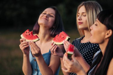 Gün batımı mavi elbiseler üç genç çekici kadın arkadaşlar karpuz yiyor ve gülümseyen.