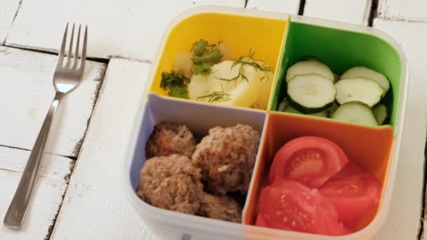 Ebéd doboz cellákkal. zöldségek, uborka és paradicsom, főtt burgonya és hústermékek. — Stock videók