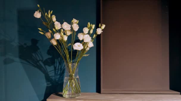 Glass vase with gently pink carnations stands on a wooden table against the background of the wall. Part of the interior. — Stock Video