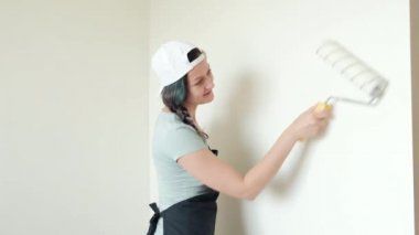 Genç kadın ev ressam bir silindir ile beyaz bir duvar boyar.