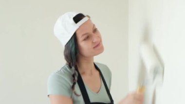 Genç kadın ev ressam bir silindir ile beyaz bir duvar boyar.