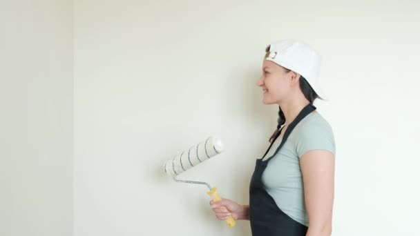 Νέος θηλυκός ζωγράφος σπίτι ζωγραφίζει ένα λευκό τοίχο με ένα ρολό. — Αρχείο Βίντεο