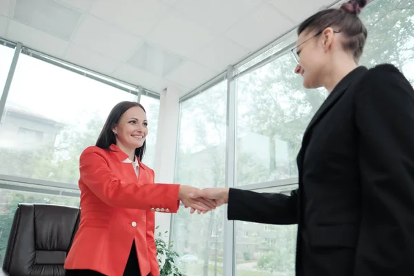 Twee mooie jonge vrouwen in business suits schudden de handen en glimlach. Een vacature inhuren. Ondertekening van de overeenkomst. Vrouwen op het werk. — Stockfoto