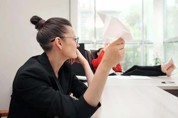 Drie mooie jonge meiden in business suits zitten aan het Bureau. Moe van het werk. Gooi papieren vliegtuigen, en lach. Pauze en rust. — Stockfoto