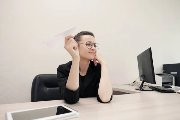 Drie mooie jonge meiden in business suits zitten aan het Bureau. Moe van het werk. Gooi papieren vliegtuigen, en lach. Pauze en rust. — Stockfoto