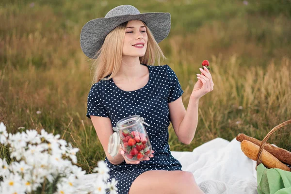 Young attractive woman in a blue dress at an outdoor picnic. A basket with daisies, watermelon, strawberries and a glass of lemonade.