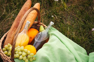 Yeşil çim üzerinde çayırda yaz pikniği. Meyve sepeti, meyve suyu ve şişe şarap, karpuz, çilek bir cam kavanoz ve ekmek Bagetler. Beyaz masa örtüsü ve bir buket alan papatyalar.