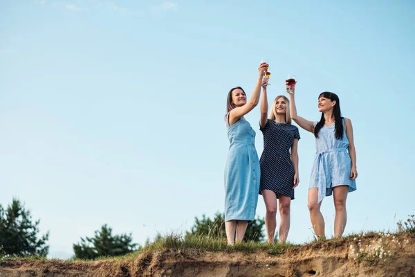 Τρεις νεαρές ελκυστικές γυναίκες, με μπλε φορέματα περπατούν κατά μήκος της ακροθαλασσιάς. Οι φιλενάδες επικοινωνούν, γελούν και πίνουν κρασί. — Φωτογραφία Αρχείου
