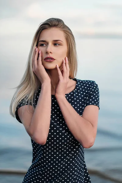 Porträt einer jungen attraktiven blonden Frau, in einem blauen Kleid im Freien, die Hände auf dem Gesicht. — Stockfoto