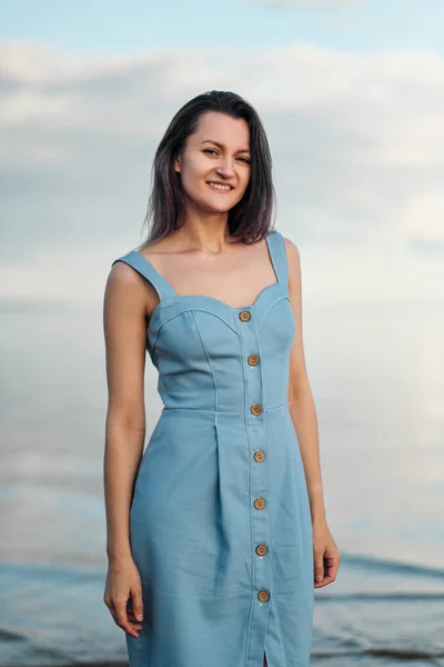 A young attractive dyed hair woman, in a blue dress, on background of seashore and sea. — Stock Photo, Image