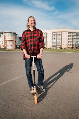 Uzun saçlı ve sakallı yaşlı bir adam şehir sokaklarında bir Scooter sürmek. Gömlek ve kot kontrol.