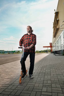 Uzun saçlı ve sakallı yaşlı bir adam şehir sokaklarında bir Scooter sürmek. Gömlek ve kot kontrol.
