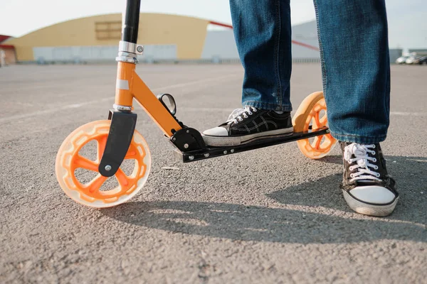 Close-up van Oranje stuntstep wielen. Benen van een man in blauwe sneakers en jeans. — Stockfoto