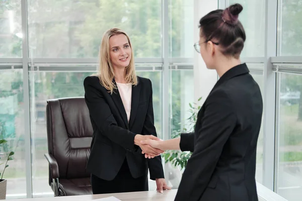 Dos hermosas mujeres jóvenes en trajes de negocios se dan la mano y sonríen. Contratar un trabajo. Firma el acuerdo. Mujeres en el trabajo . — Foto de Stock