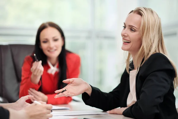 Tres mujeres jóvenes y atractivas en trajes de trabajo están sentadas en un escritorio y discutiendo los flujos de trabajo. Cabeza y subordinados. Equipo de trabajo de profesionales y colegas . — Foto de Stock