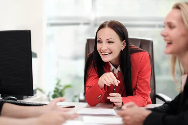 Tres mujeres jóvenes y atractivas en trajes de trabajo están sentadas en un escritorio y discutiendo los flujos de trabajo. Cabeza y subordinados. Equipo de trabajo de profesionales y colegas . — Foto de Stock