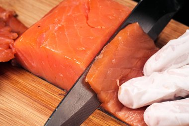 Eller yakın çekim pişirir. Şef bıçakla keser kırmızı balık, tahtalı bir kesme tahtasında somon füme.