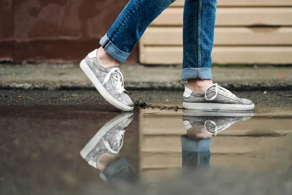 Close-up of feet in sneakers are walking through the puddles on the pavement. — Stock Photo, Image