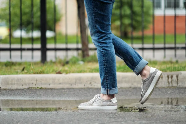 Primer plano de los pies en zapatillas de deporte están caminando a través de los charcos en el pavimento . — Foto de Stock