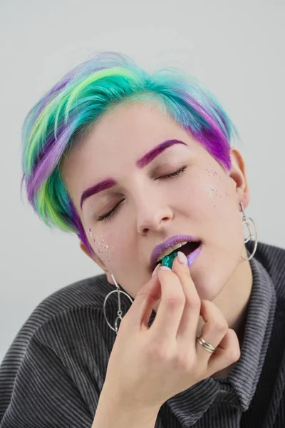 A young woman with short pixie bob haircut and dyed hair, holds in the mouth and in the hands gemstones and jewels. — Stock Photo, Image