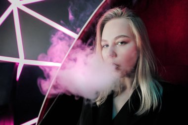 Güzel genç kadın sarışın neon mor ışıklar arka planda bir gece kulübünde bir nargile duman nefes.