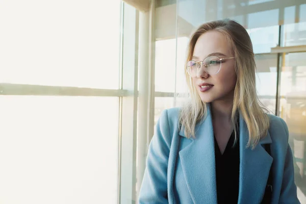 一个戴着眼镜、穿着蓝色外套的年轻漂亮女孩在玻璃电梯里的肖像. — 图库照片