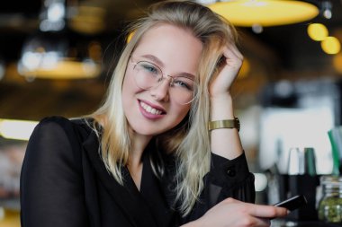 Gözlüklü genç ve güzel sarışın bir kadın barda sarı bir iç mekanda oturuyor. Bir saman ve yeşil nane ile Içecekler alkollü kokteyl.