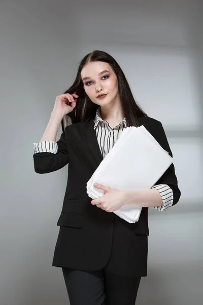 Ung vacker kvinnlig mode modell i ett företag snygg kostym på en rerom bakgrund. Innehåller en bunt papper och en penna. — Stockfoto