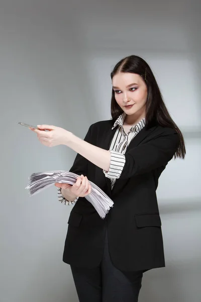 Joven modelo de moda femenina hermosa en un traje de negocios con estilo en un fondo rerom. Sostiene una pila de papeles y una pluma . — Foto de Stock