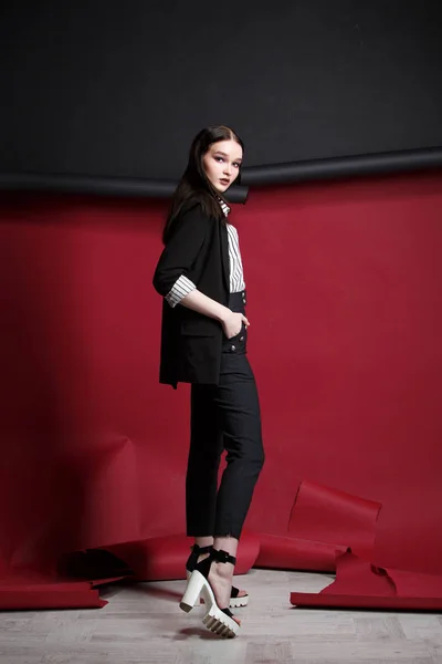 Young beautiful female fashion model in a business stylish suit on a red and black background. — Stock Photo, Image