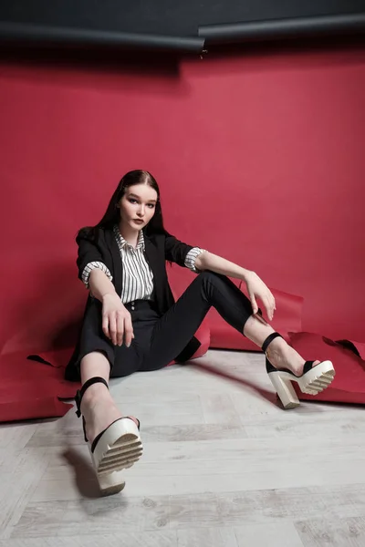 Jovem modelo de moda feminina bonita em um terno elegante de negócios em um fundo vermelho e preto . — Fotografia de Stock