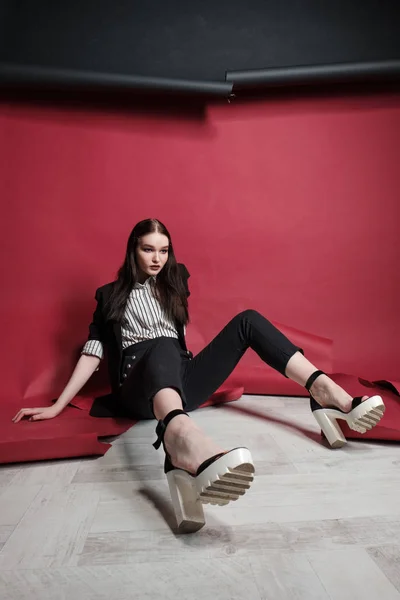 Young beautiful female fashion model in a business stylish suit on a red and black background. — Stock Photo, Image