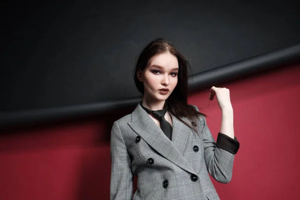 Jovem modelo de moda feminina bonita em um terno elegante de negócios em um fundo vermelho e preto . — Fotografia de Stock
