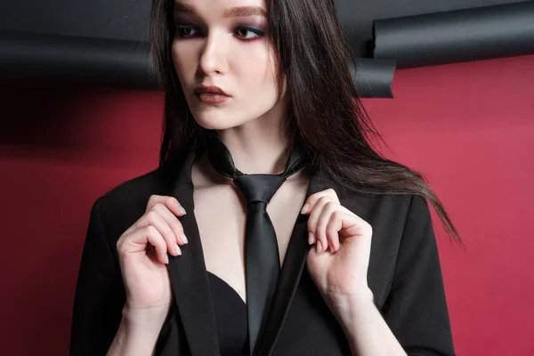 Young beautiful female fashion model in a business stylish suit on a red and black background. — Stock Photo, Image