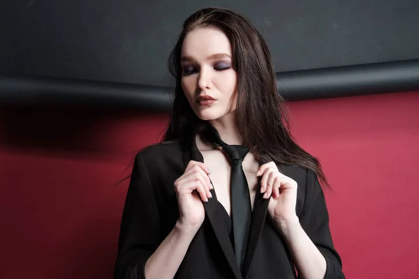 Young beautiful female fashion model in a business stylish suit on a red and black background. — Stock Photo, Image