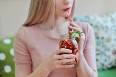 Pembe elbiseli genç güzel sarışın kız bir kafe masasında oturur, cam bir kavanozdan limonata içer.