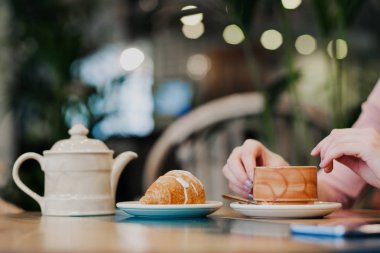Bir kafede kahvaltı. Çay ve kruvasan ile kahverengi seramik fincan masada.