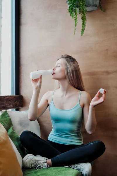 Ahşap bir duvarın arka planına karşı bir kafenin penceresinde oturan spor genç güzel atletik kadın sarışın.