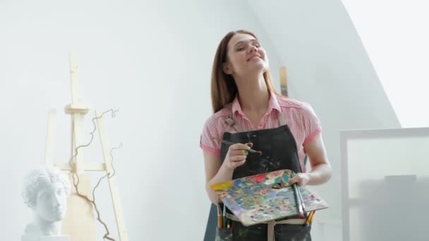 Young beautiful woman painter among easels and canvases in a bright studio. — Stock Video