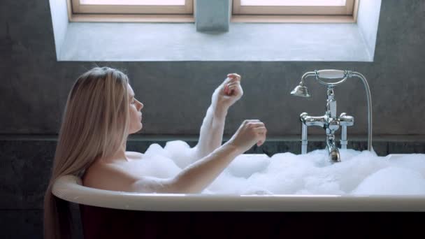 Belle femme blonde se trouve dans un bain avec de la mousse et se détend . — Video