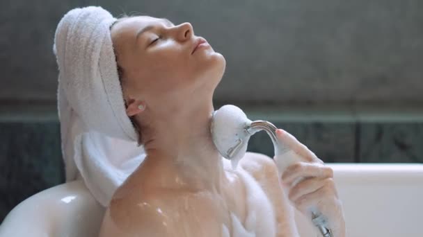 Vacker blond kvinna ligger i ett bad med skum och slappnar. Vit handduk på huvudet. — Stockvideo