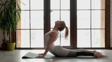 Beyaz spor genç güzel atletik kadın sarışın yoga yapıyor ve çok katlı binanın büyük pencerenin arka planda gri bir halı üzerinde uzanan.