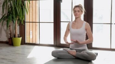 Genç bir güzel atletik kadın sarışın yere oturur ve kollarını göğsüne katlanmış nefes.