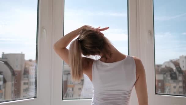 年轻的美丽的运动女人金发女郎在白色运动服做瑜伽和伸展在阳台上在家里。站在手指上，表演舞步. — 图库视频影像