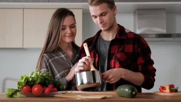 Νεαρό όμορφο ζευγάρι σε καρό πουκάμισα μαγειρεύουν στο σπίτι στην κουζίνα. — Αρχείο Βίντεο