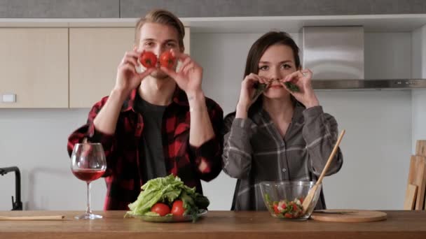 격자 무늬 셔츠에 젊은 아름다운 부부는 부엌에서 집에서 요리하고 있습니다. 여자와 남자는 야채를 잘라 투명 유리 접시에 후추, 토마토, 무의 샐러드를 만들. — 비디오