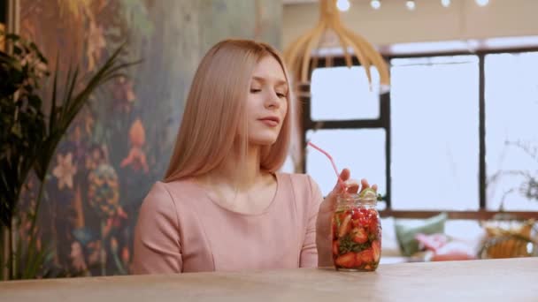 Junge schöne Mädchen trinkt Erdbeer-Limonade aus einem Glas mit einem Strohhalm hinter der Theke. — Stockvideo