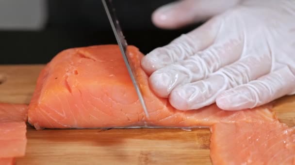 Młody mężczyzna szef kuchni Sushi tnie wędzony filet z łososia nożem na stole. Ręce w rękawicach zbliżenie. — Wideo stockowe