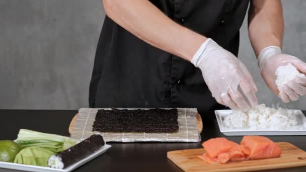 Giovane chef di sushi maschile prepara panini di sushi giapponesi di riso, salmone, avocado e nori. Ristorante cucina . — Video Stock