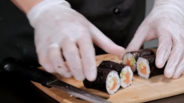 Le jeune chef sushi prépare des rouleaux japonais de riz, saumon, avocat et nori. Restaurant cuisine, mains closeup . — Video